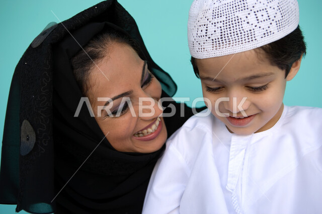 مسؤولية المرأة تجاه أولادها, دور الأم في تربية أبنائها والعناية بهم, بورتريه مقرب لأم عربية إماراتية خليجية ترتدي العباءة والحجاب تنظر إلى طفلها بإيماءات الحب والحنان, مفهوم الطفولة والأمومة, قضاء أوقات ممتعة مع الأبناء, خلفية زرقاء