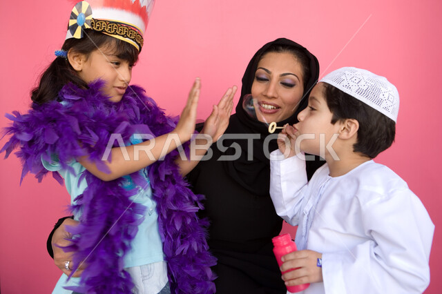 Playing with water bubbles with gestures of happiness and joy, spending time with fun recreational activities, a portrait of an Emirati Arab family enjoying making soap bubbles, developing children's motor skills, the concept of a happy family, cultivatin