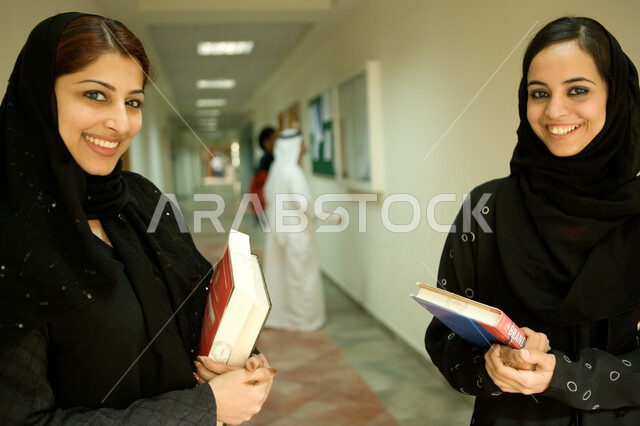 مشاركة الآراء في اختيار الروايات, تنمية الأفكار واكتساب المعلومات من خلال قراءة الكتب، إجراء مسابقات في قراءة القصص التثقيفيه والتعليمية ، صورة مقربة لطالبتان عربيتان اماراتيتان محجبتان يرتديان العباءة السوداء ينظران إلى الكاميرا بإيماءات السعادة