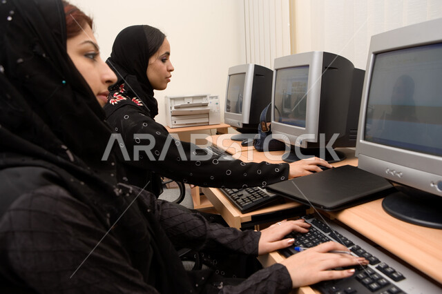 Teaching students how to use computer technologies in universities, practical application for students in computer rooms, advanced curricula and e-learning in the Emirates, a close-up of two Arab Gulf Emirati students sitting in a computer room and doing 