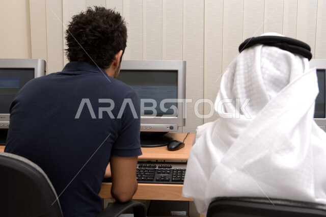 المناهج المتطورة والتعليم الالكتروني، مدارس أكاديمية في الإمارات، التطبيق العملي للطلاب، تعليم الطلبة كيفية استخدام تقنيات الكمبيوتر في المدرسة، صورة مقربة من الخلف لطالبان عربيان خليجيان إماراتيان يقومان بالكتابة على لوحة المفاتيح في غرفة الحواسيب.