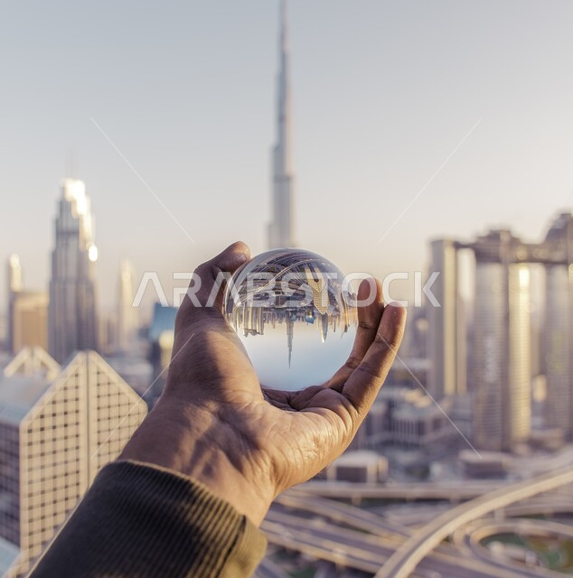 صورة مقربة ليد رجل يحمل كرة بلورية بانعكاس أفق دبي وناطحات السحاب في الإمارات العربية المتحدة في وضح النهار, شبكة المواصلات والطرقات والشوارع الرئيسية, مفهوم الهندسة المعمارية الحديثة في المنشآت السكنية و التجارية.