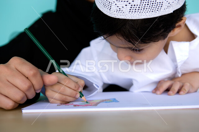 Fun artistic entertainment activities, developing children's skills and nurturing them, a close-up portrait of an Arab Gulf Emirati child wearing Emirati dress drawing and coloring with his mother, learning and passion for drawing with gestures of focus a