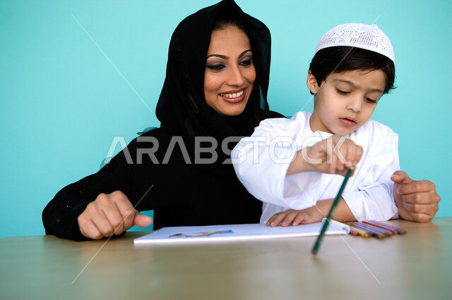 Entertainment and artistic activities, developing and caring for children's skills, a portrait of an Arab Gulf Emirati child wearing Emirati dress drawing and coloring with his mother, learning and the passion of love for drawing, a mother helping her son