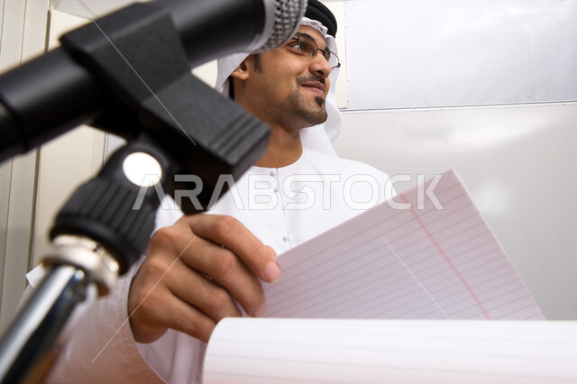 الشرح والتعليم والإجابه على أسئلة الطلاب، الندوات التعليمية التثقيفيه المفيده، صورة مقربة لأستاذ جامعي اماراتي عربي خليجي مبتسم يتحدث على المايكرفون و يقوم بإلقاء عرض تقديمي , التعليم الجامعي في الامارات العربيه المتحده