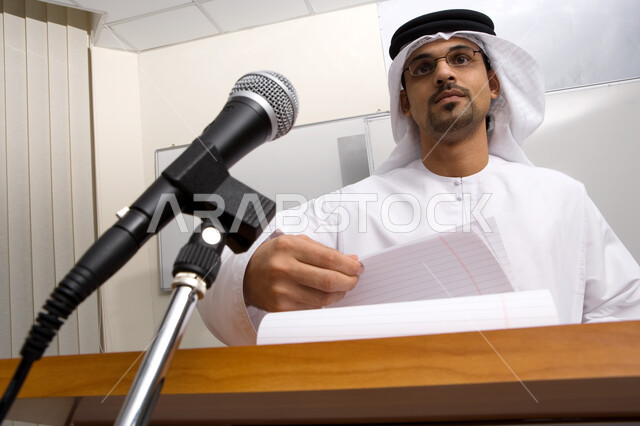 التعليم الجامعي في الامارات العربيه المتحده، الندوات التعليمية التثقيفيه المفيده، صورة مقربة لأستاذ جامعي اماراتي عربي خليجي مبتسم يتحدث على المايكرفون و يقوم بإلقاء عرض تقديمي