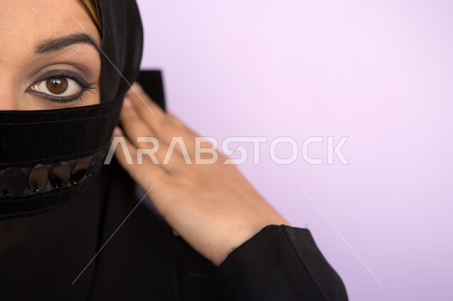  نظرات الأنوثه الناعمه، ابراز العين السوداء المكحله ، مفهوم الحياء والستر، بورتريه مقرب لوجه امراه عربية اماراتيه خليجيه محجبه تقوم بوضع اللثام على وجهها ، النظر الى الكاميرا، خلفية ملونه