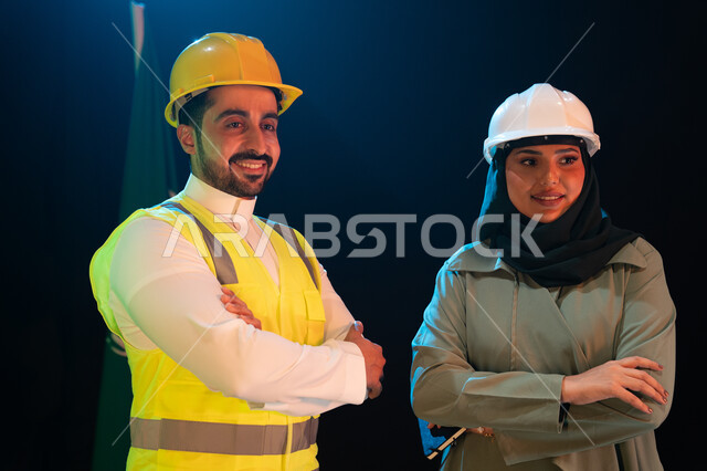 Saudi Flag Day March 11th, engineering development and development of the construction sector with the hands of the people of the homeland, a close-up portrait of two smiling Saudi Arabian Gulf engineers wearing protection helmets standing with crossed ha