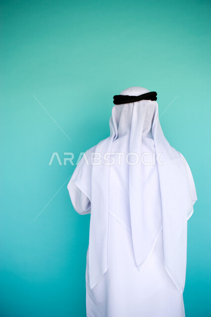 الاهتمام بالمظهر الخارجي, الوقوف باستقامة وثقة, بورتريه من الخلف لرجل عربي خليجي امارتي يرتدي الكندورة والغترة الاماراتية , خلفية زرقاء