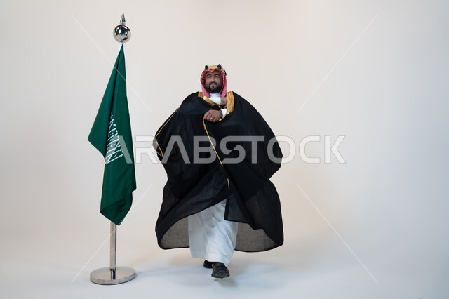 تأسيس المملكة العربية السعودية 1727 م، ذكرى اليوم الوطني السعودي 23 سبتمبر، يوم العلم 11 مارس، بورتريه لرجل عربي خليجي سعودي يرتدي البشت والشماغ يقف بجانب البيرق، مؤسس الدوله السعوديه الاولى الامام محمد بن سعود، صورة الجسم بالطول الكامل، خلفية بيضاء