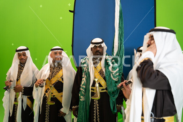 يوم العلم السعودي 11 مارس ،عروض و فنون الفلكلور التراثي السعودي، فرقة العرضة النجدية في المناسبات الوطنية، صورة مقربة لرجل عربي خليجي سعودي يرتدي الغترة والدقله يضع يده على أذنيه، الاحتفال بذكرى اليوم الوطني السعودي 23 سبتمبر ، خلفية خضراء وزرقاء، كروما