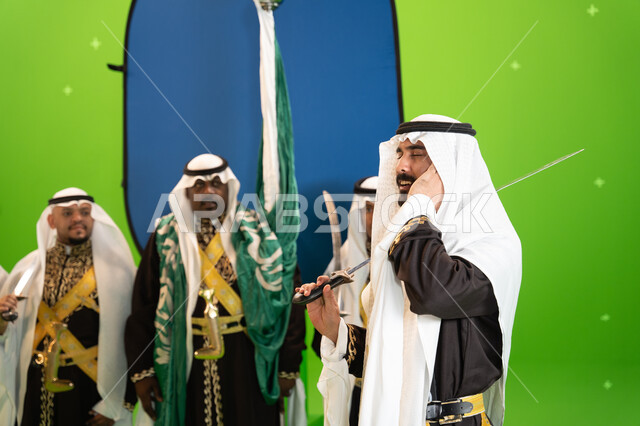 عروض و فنون الفلكلور التراثي السعودي، فرقة العرضة النجدية في المناسبات الوطنية، يوم العلم السعودي 11 مارس ، صورة مقربة لرجل عربي خليجي سعودي يرتدي الغترة والدقله يضع يده على أذنيه، الاحتفال بذكرى اليوم الوطني السعودي 23 سبتمبر ، خلفية خضراء وزرقاء، كروما