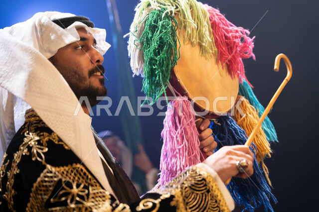 Interaction and participation in national holidays and events, a close-up photo from the side of a Saudi Gulf Arab man wearing the traditional Najdi Ardha dress celebrating National Day on September 23, Saudi Flag Day on March 11, traditional folklore ban