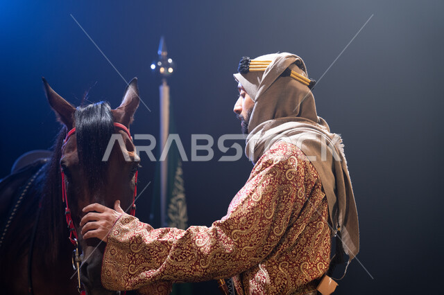 يوم العلم السعودي 11 مارس، الوقوف بجانب علم السعودية باعتزاز، اليوم الوطني23 سبتمبر، المناسبات والأعياد الوطنية، ذكرى تأسيس الدولة السعودية الأولى 1727 م، صورة جانبية لرجل خليجي يرتدي الدقلة والغترة يقف مع خيله العربي الأصيل، خلفية ضبابية مع إضاءة بيضاء. 