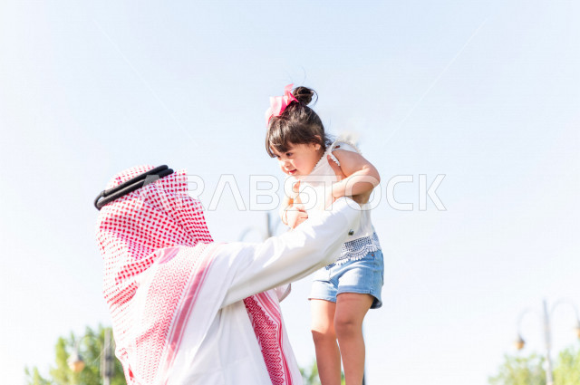 A beautiful girl with Down syndrome spends her time outing with her father in the park, a Saudi Gulf father plays with his daughter outdoors, people of determination, people with special needs