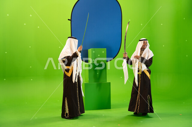 الاهازيج والرقصات بالاحتفال بذكرى تأسيس الدولة السعودية الاولى 22 شباط ، إظهار إرث المنطقة الجنوبية, استخدام السيوف في الرقص الشعبي، رجلان عربيان سعوديان من فرقة العرضة النجديه يرتديان الغترة والدقله، صورة الجسم بالطول الكامل، خلفيه خضراء و زرقاء ،كروما