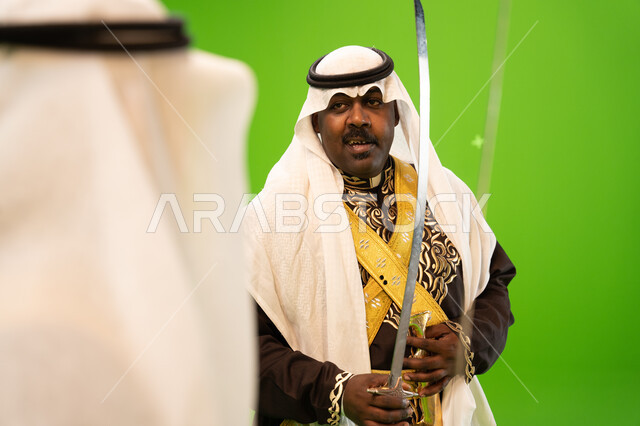 الفعاليات والرقصات الشعبية و الأهازيج في العرضة النجدية في المناسبات الوطنية، الاحتفال بذكرى اليوم الوطني السعودي ،العيد الوطني السعودي 23 سبتمبر، صورة مقربة لرجل عربي خليجي سعودي يرتدي الغترة والدقلة يرقص بالسيف، خلفية خضراء ،كروما