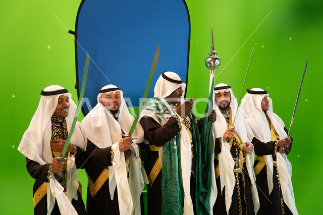 إرتداء ازياء العرضة النجدية الشعبية، إظهار التراث السعودي العربي ،صورة مقربة لفرقة العرضة النجدية في الاحتفالات و المناسبات الوطنية، الاحتفال بذكرى اليوم الوطني السعودي 23 سبتمبر ، صورة الجسم بالطول الكامل، خلفية خضراء وزرقاء، كروما