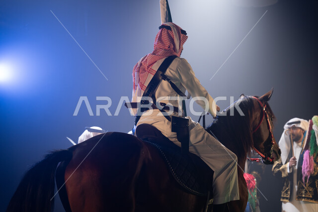 فعاليات ركوب الخيل في الأعياد السعودية, مشاركة الأحصنة في الاحتفالات الوطنية, صورة من الخلف لفارس عربي خليجي سعودي يمتطي فرسة ويمسك علم المملكة بفخر واحترام, عروض فرقة الفلكلور التراثي في اليوم الوطني 23 سبتمبر, يوم العلم السعودي 11 مارس