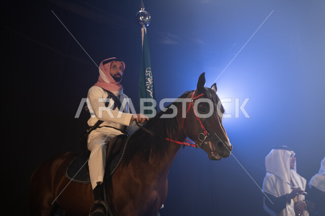 أنشطة وفعاليات ركوب الخيل في الأعياد السعودية, مشاركة الأحصنة في الاحتفالات الوطنية, فارس عربي خليجي سعودي يمتطي فرسة ويمسك علم المملكة بفخر واحترام, عروض فرقة الفلكلور التراثي في اليوم الوطني 23 سبتمبر, يوم العلم السعودي 11 مارس, ارتداء زي العرضة النجدية
