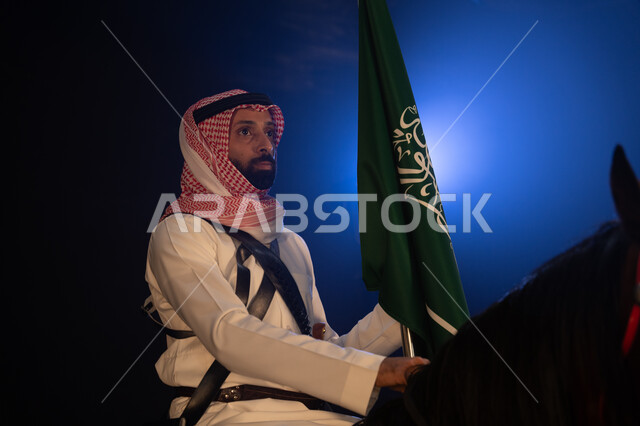 العيد الوطني السعودي 8 ربيع الاول، الاحتفال مع الخيول في الأعياد والمناسبات الوطنية، نشر حب الخيل بين ابناء الوطن، ذكرى يوم العلم السعودي 11 مارس، شاب عربي سعودي يرتدي الشماغ والزي التقليدي يمسك علم السعودية يمتطي فرسه في الليل