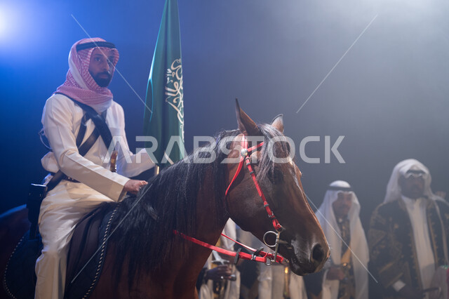 Participation of horses in national celebrations, a Saudi Arabian Gulf horseman riding a horse and holding the Kingdom’s flag with pride and respect, horse riding activities and events on Saudi holidays, traditional folklore band performances on National 