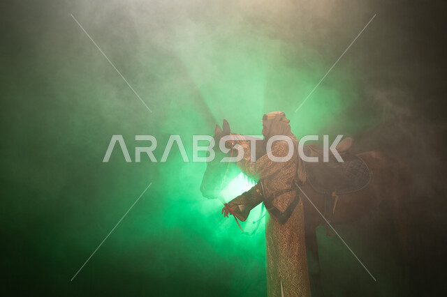 ارتداء أزياء المناسبات والأعياد الوطنية، نشر حب الخيل بين أبناء الوطن، ذكرى تأسيس الدولة السعودية الأولى 1727 م، يوم التأسيس السعودي 22 فبراير، صورة جانبية لرجل خليجي يرتدي الدقلة والغترة يداعب خيله العربي الأصيل، خلفية ضبابية مع إضاءة خضراء. 