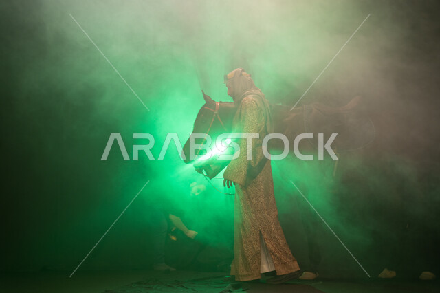 ارتداء أزياء المناسبات والأعياد الوطنية، نشر حب الخيل بين أبناء الوطن، ذكرى تأسيس الدولة السعودية الأولى 1727 م، يوم التأسيس السعودي 22 فبراير، صورة جانبية لرجل خليجي يرتدي الدقلة والغترة يداعب خيله العربي الأصيل، خلفية ضبابية مع إضاءة خضراء. 