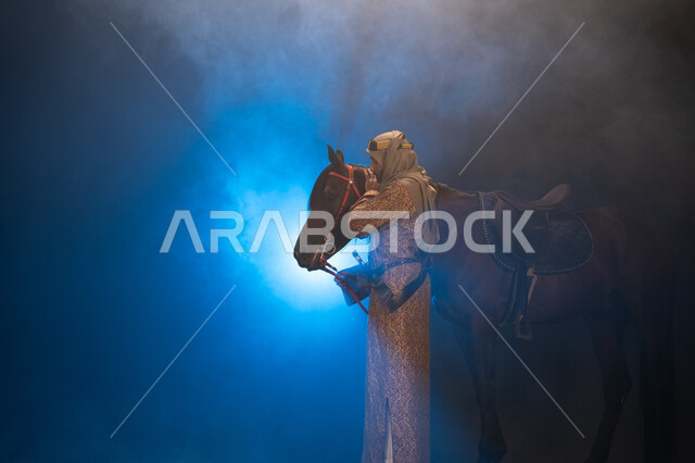 نشر حب الخيل بين أبناء الوطن، ذكرى تأسيس الدولة السعودية الأولى 1727 م، يوم التأسيس السعودي 22 فبراير، ارتداء أزياء المناسبات والأعياد الوطنية، صورة جانبية لرجل خليجي يرتدي الدقلة والغترة يداعب خيله العربي الأصيل، خلفية ضبابية مع إضاءة زرقاء. 