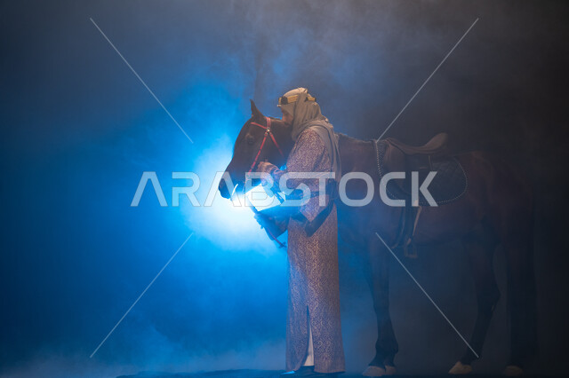 نشر حب الخيل بين أبناء الوطن، ذكرى تأسيس الدولة السعودية الأولى 1727 م، يوم التأسيس السعودي 22 فبراير، ارتداء أزياء المناسبات والأعياد الوطنية، صورة جانبية لرجل خليجي يرتدي الدقلة والغترة يداعب خيله العربي الأصيل، خلفية ضبابية مع إضاءة زرقاء. 