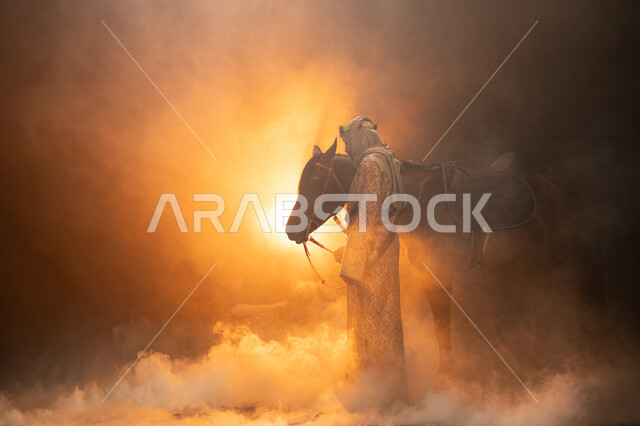 ذكرى تأسيس الدولة السعودية الأولى 1727 م، يوم التأسيس السعودي 22 فبراير، حب الفروسية والشغف في تربية الجياد، ارتداء أزياء المناسبات والأعياد الوطنية، صورة جانبية لرجل خليجي يرتدي الدقلة والغترة يداعب خيله العربي الأصيل، خلفية ضبابية مع إضاءة صفراء. 