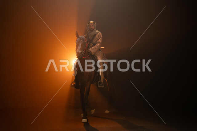 الاحتفال مع الخيل بذكرى تأسيس الدولة السعودية الأولى 1727 م، يوم التأسيس السعودي 22 فبراير، ممارسة هواية ركوب الأحصنة، ارتداء أزياء المناسبات والأعياد الوطنية، رجل خليجي يرتدي الدقلة والغترة يمتطي فرسه البني العربي الأصيل، خلفية ضبابية مع إضاءة صفراء. 