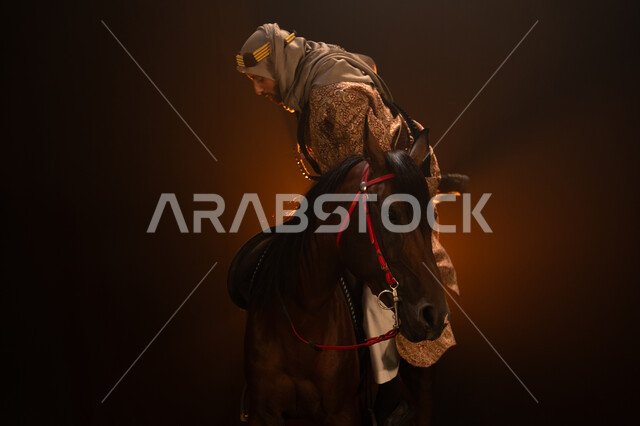 الاحتفال مع الخيل بذكرى تأسيس الدولة السعودية الأولى 1727 م، يوم التأسيس السعودي 22 فبراير، ممارسة هواية ركوب الأحصنة، ارتداء أزياء المناسبات والأعياد الوطنية، رجل خليجي يرتدي الدقلة والغترة يمتطي فرسه البني العربي الأصيل، خلفية ضبابية مع إضاءة صفراء. 