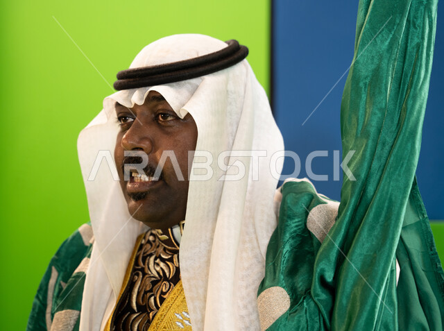 إحياء الفلكلور السعودي في الاحتفال بذكرى اليوم الوطني السعودي 23 سبتمبر، يوم العلم السعودي11 مارس، صورة مقربة لرجل سعودي يقوم بإلقاء القصائد الحماسيه والشعر ، ارتداء ازياء العرضة النجدية، تأسيس الدولة السعودية الأولى 1727 م، خلفية خضراء وزرقاء، كروما