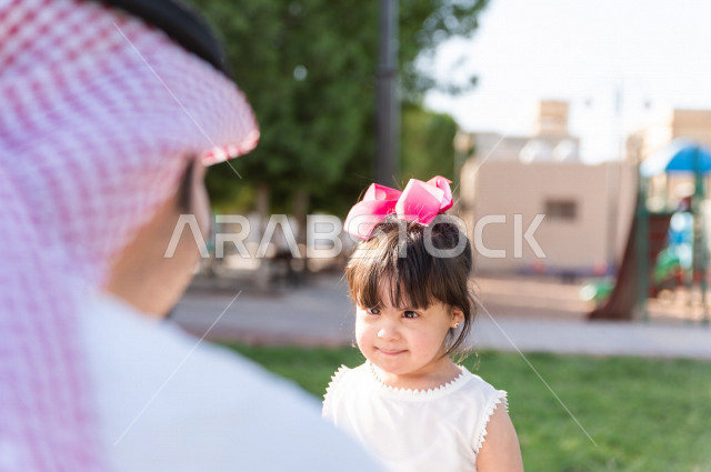 A beautiful girl with Down syndrome spends her time outing with her father in the park, a Saudi Gulf father plays with his daughter outdoors, people of determination, people with special needs
