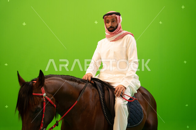 اتباع تقاليد الاجداد برعاية وتربية الجياد والاهتمام بها، بورتريه مقرب لرجل عربي خليجي سعودي يرتدي الثوب التقليدي والشماغ يمتطي خيل بني عربي أصيل، حب وعشق الاحصنة، ممارسة هواية ركوب الخيل وشغف الفروسية، خلفية خضراء، كروما