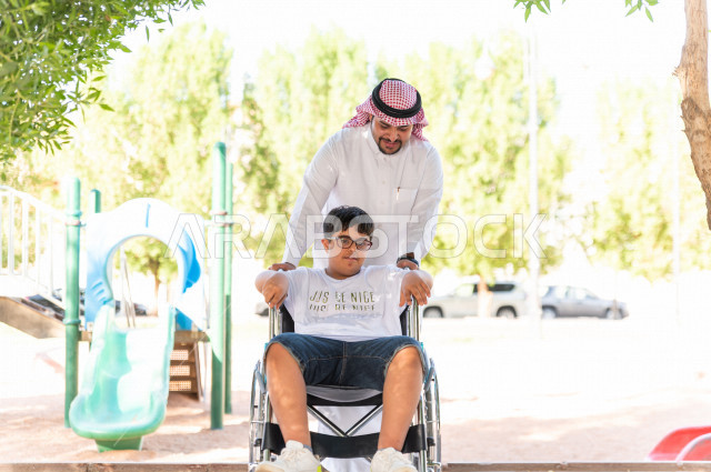 ولد جميل سعوي خليجي مصاب بملازمة داون يقضي وقته في نزهه مع والده  بالمنتزه ، طفل مقعد على كرسي متحرك يستمتع بالهواء الطلق ، أصحاب الهمم ، ذوي الاحتياجات الخاصة ، اعاقة حركية