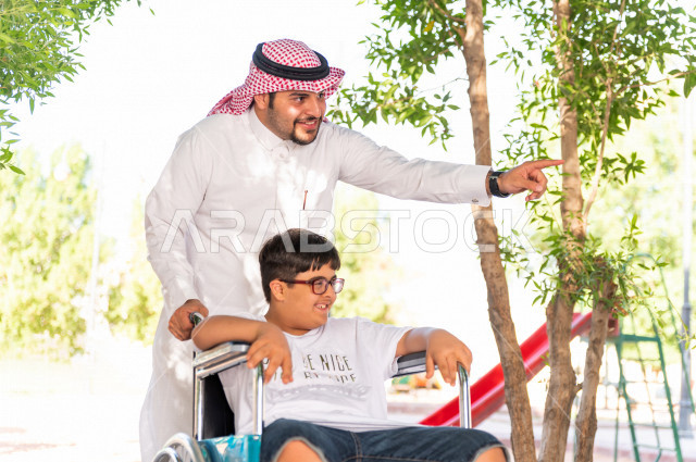 ولد جميل سعوي خليجي مصاب بملازمة داون يقضي وقته في نزهه مع والده  بالمنتزه ، طفل مقعد على كرسي متحرك يستمتع بالهواء الطلق ، أصحاب الهمم ، ذوي الاحتياجات الخاصة ، اعاقة حركية