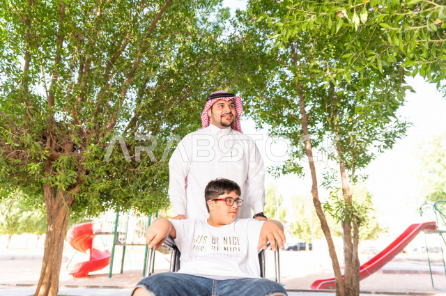 ولد جميل سعوي خليجي مصاب بملازمة داون يقضي وقته في نزهه مع والده  بالمنتزه ، طفل مقعد على كرسي متحرك يستمتع بالهواء الطلق ، أصحاب الهمم ، ذوي الاحتياجات الخاصة ، اعاقة حركية