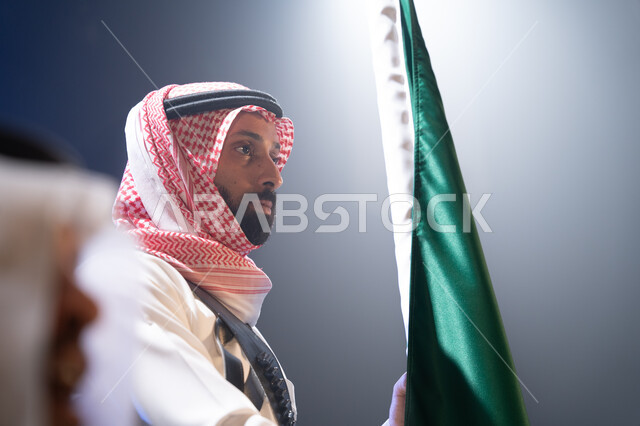 النظر إلى شيء ما، الاحتفالات والمناسبات الوطنية, صورة مقربة لرجل عربي خليجي يرتدي الزي السعودي يحتفل باليوم الوطني 23 سبتمبر في وقت الليل,  ذكرى يوم العلم السعودي 11 مارس، خلفية سوداء مع إضاءة بيضاء.