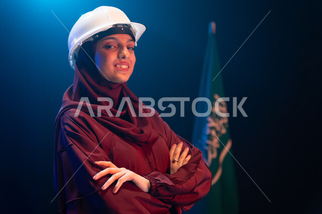 العمل في القطاع الهندسي السعودي، مهن ووظائف نسائية، صورة مقربة لمهندسة عربية خليجية سعودية مبتسمة ترتدي الحجاب وخوذة الحماية البيضاء تقف بجانب علم السعودية، الاحتفال في يوم العلم 11 مارس، ذكرى اليوم الوطني السعودي 23 سبتمبر، خلفية سوداء مع اضاءة بيضاء