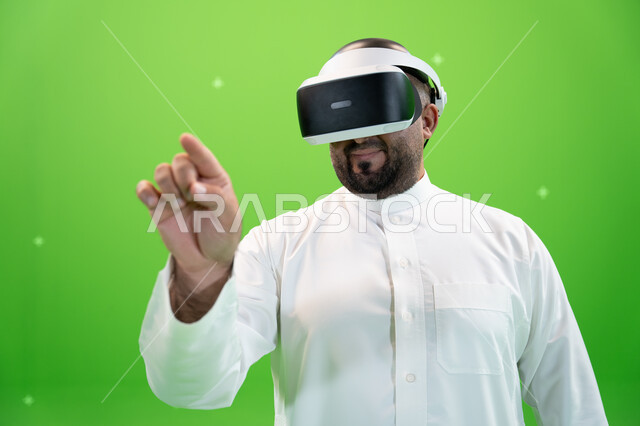 الضغط على شاشه هولوجراميه باصبع السبابه، بورتريه مقرب  لرجل عربي خليجي سعودي يرتدي الزي التقليدي يلبس نظارة الواقع الإفتراضي ثلاثية الأبعاد، خلفية خضراء، كروما