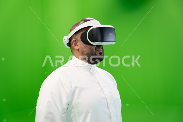 استخدام التقنيات الحديثة المتطورة في مشاهدة الأفلام و محاكاة العالم الخيالي ،التسليه والترفيه في أوقات الفراغ، بورتريه مقرب لرجل عربي خليجي سعودي يرتدي الزي التقليدي يلبس نظارة الواقع الإفتراضي ثلاثية الأبعاد، خلفية خضراء، كروما