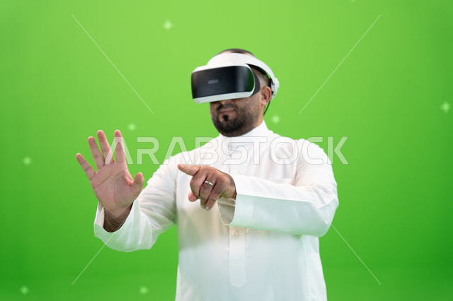 ارتداء نظارة الواقع الإفتراضي ثلاثية الأبعاد ،ايماءات تدل على دفع عنصر هولوجرامي، بورتريه مقرب  لرجل عربي خليجي سعودي يرتدي الزي التقليدي يرفع اصبع السبابة للنقر على شاشه هولوجرامية، خلفية خضراء، كروما