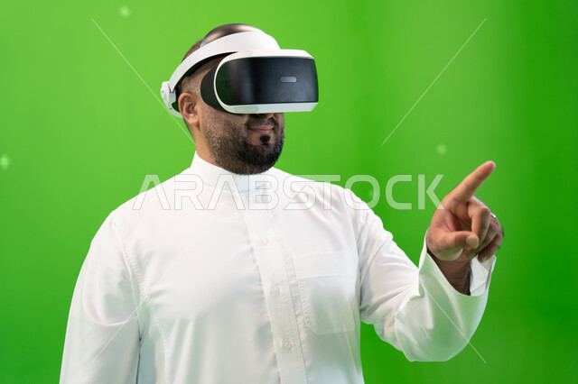 Clicking on the hologram screen with the index finger, a close-up portrait from the side of a Saudi Gulf Arab man wearing traditional clothing, wearing 3D virtual reality glasses, green background, chroma