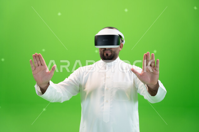 علامات يدين تدل على الاحساس و اللمس و دفع عنصر هولوجرامي، بورتريه مقرب لرجل عربي خليجي سعودي يرتدي الزي التقليدي يلبس نظارة الواقع الإفتراضي ثلاثية الأبعاد، خلفية خضراء، كروما