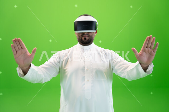 علامات يدين تدل على اللمس و دفع عنصر هولوجرامي و اللمس، بورتريه مقرب  لرجل عربي خليجي سعودي يرتدي الزي التقليدي يلبس نظارة الواقع الإفتراضي ثلاثية الأبعاد، خلفية خضراء، كروما