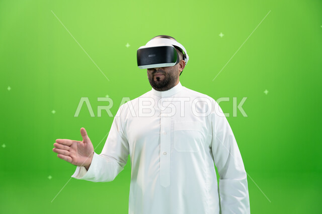 استخدام  التقنيات الحديثة المتطورة  في مشاهدة الأفلام و محاكاة العالم الخيالي ، بورتريه مقرب لرجل عربي خليجي سعودي يرتدي الزي التقليدي يلبس نظارة الواقع الإفتراضي ثلاثية الأبعاد، ايماءات التفاعل والاندماج ، اشارات التحيه والسلام, خلفية خضراء، كروما