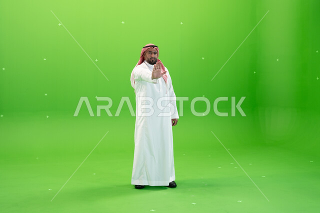 اشارات يدين تدل على النهي  عن فعل شيء ما , الصمت و التوقف عن الكلام، بورتريه لرجل عربي خليجي سعودي يرتدي الثوب والشماغ التقليدي يقوم برفع كفه للأعلى،  صورة الجسم بالطول الكامل، خلفية خضراء، كروما