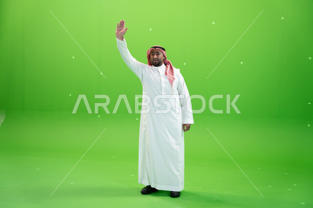 اشارات يدين تدل على إلقاء التحية والسلام و السعادة بالترحيب، بورتريه لرجل عربي خليجي سعودي يرتدي الثوب والشماغ التقليدي يقوم برفع يده اليمنى للأعلى ، صورة الجسم بالطول الكامل،  خلفية خضراء، كروما